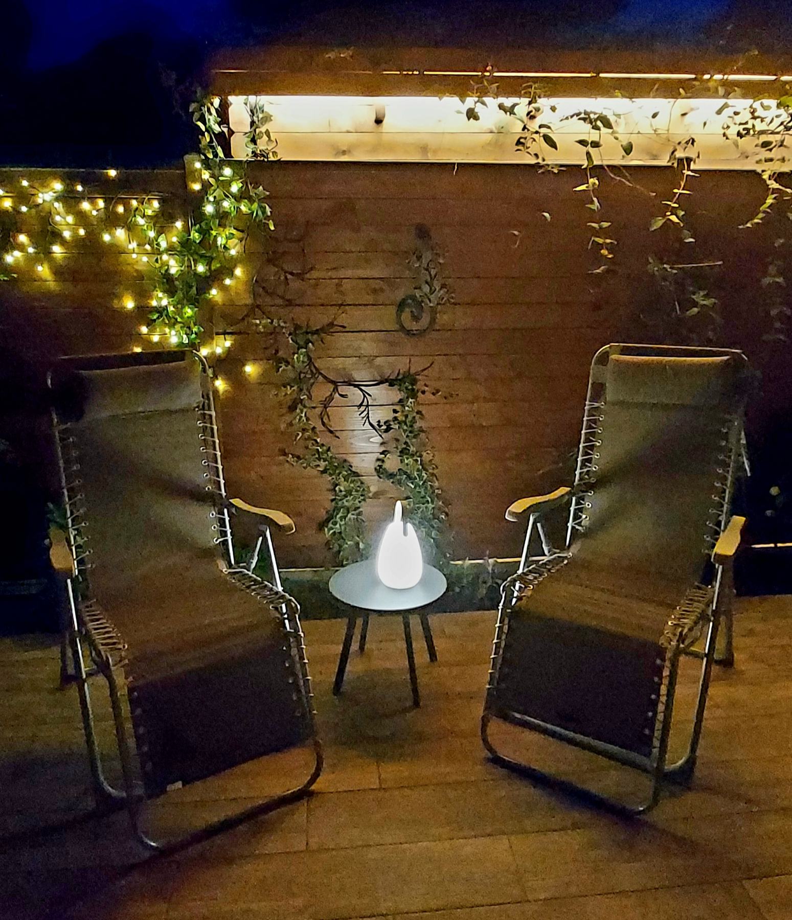 La terrasse de la résidence le soir, chaises longues et guirlande lumineuse sur la palissade en bois